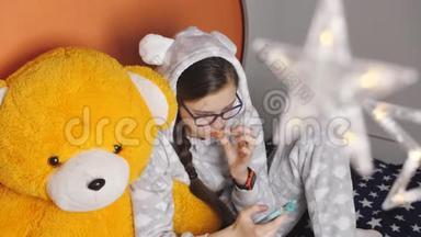 在一个寒冷的冬夜，穿着温暖的睡衣的女孩，坐在一只大泰迪熊的怀里，吃着橘子和睡衣